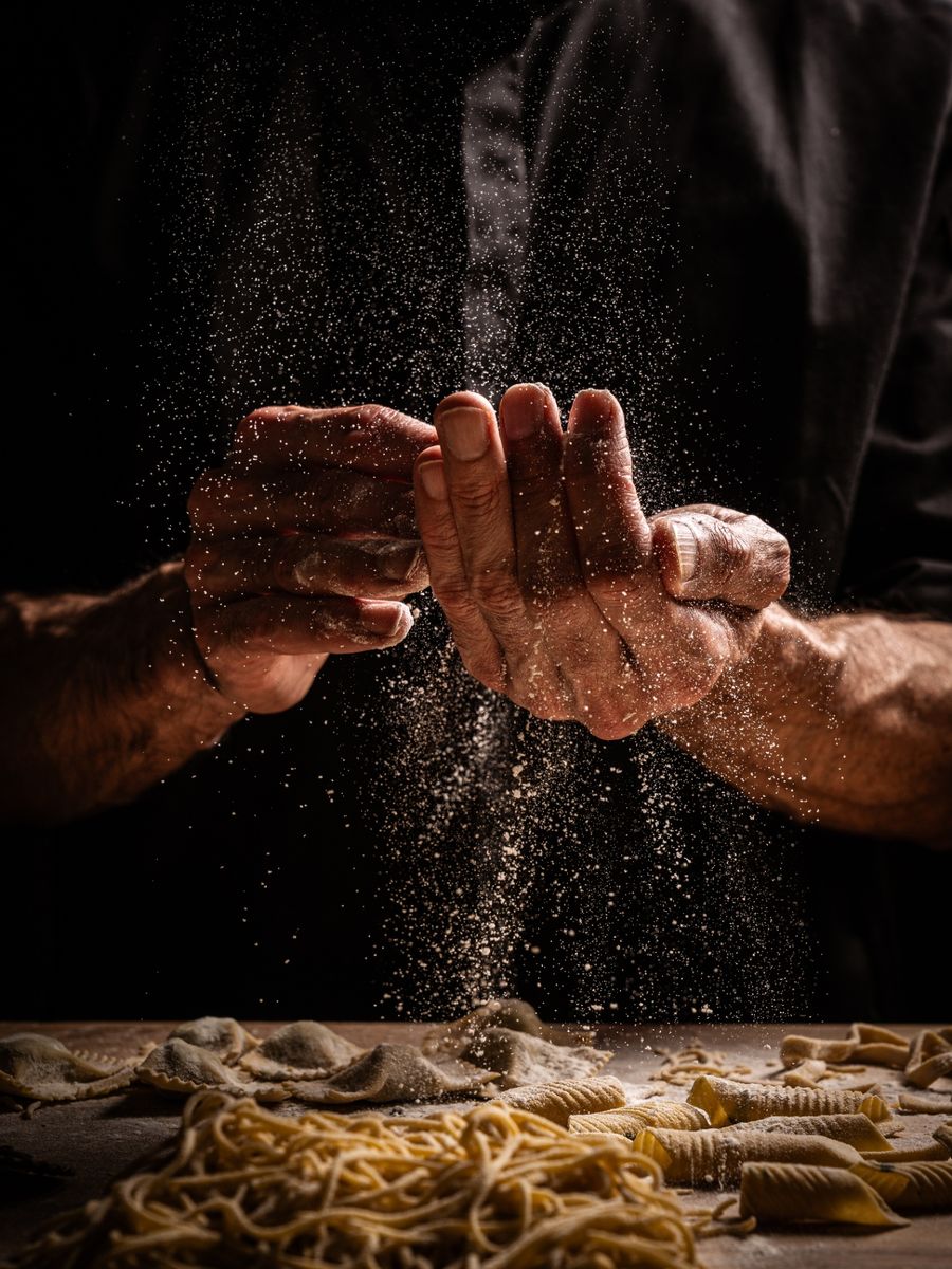 Chef's flour-dusted hands above freshly made pasta on a dark table