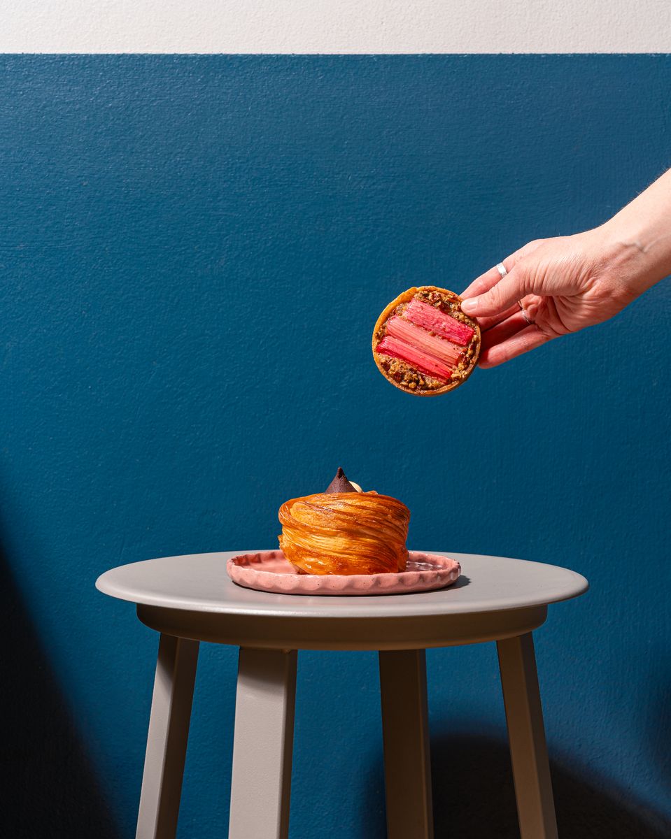 Pastry chef presenting two artisan pastries against a deep blue wall